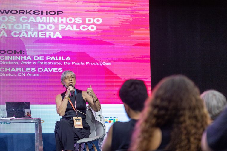 Workshop com palestrante ao microfone e telão rosa ao fundo